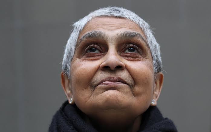 Gayatri with her grey short hair is in close up and we look up to her and her steadfast expression