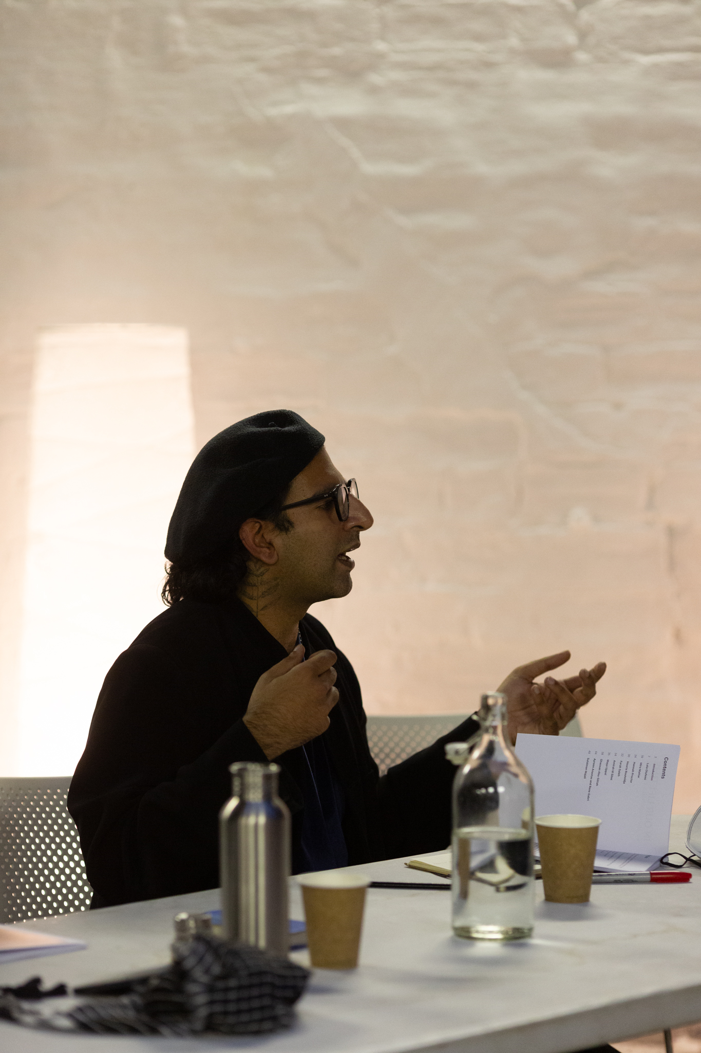 Side profile of Hussein Mitha, they are mid talking, expressively using their hands
