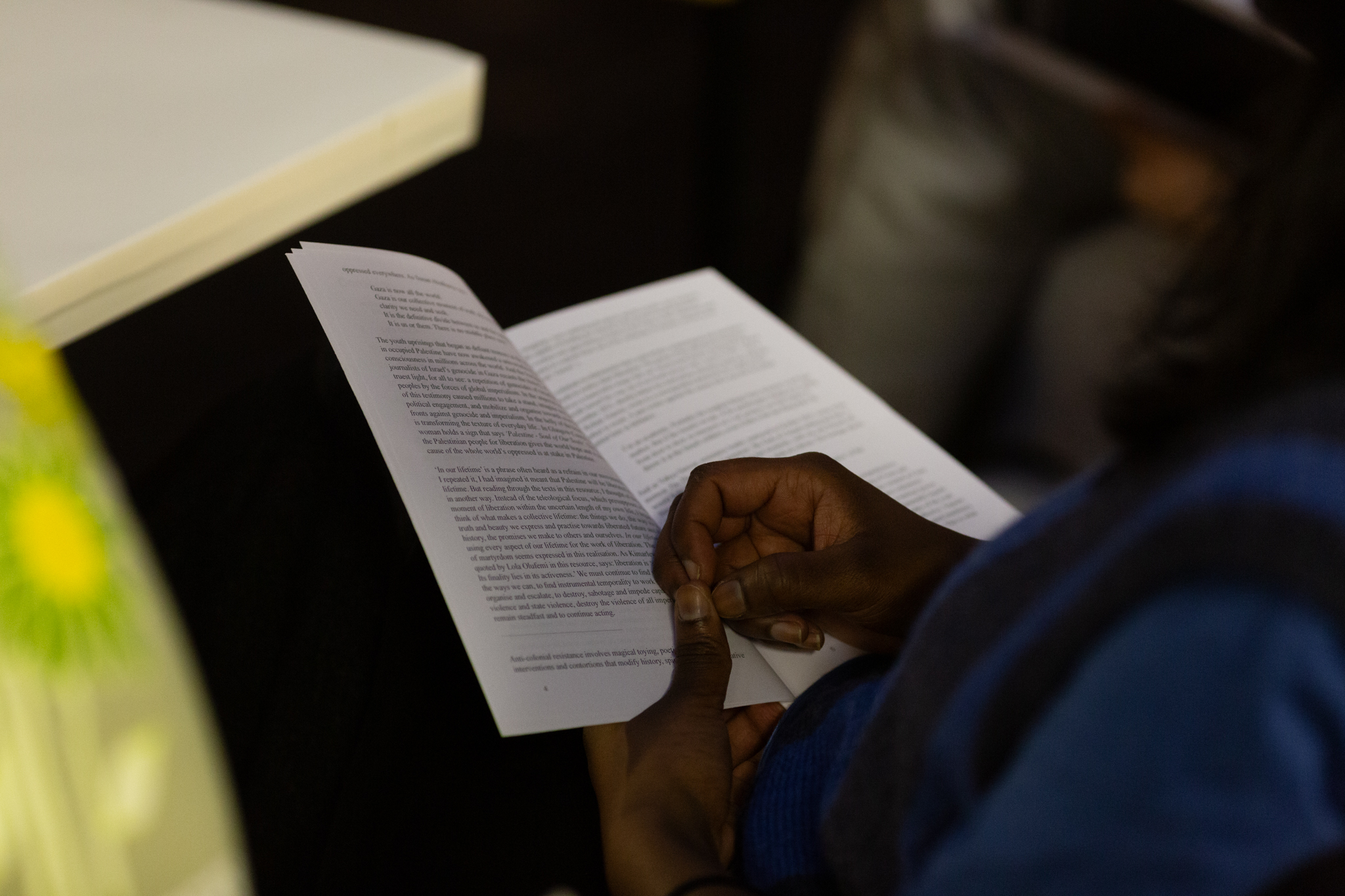close-up of a persons hands holing a white book filled with writing. One hand holds the book while the other rests on it with closed fingers