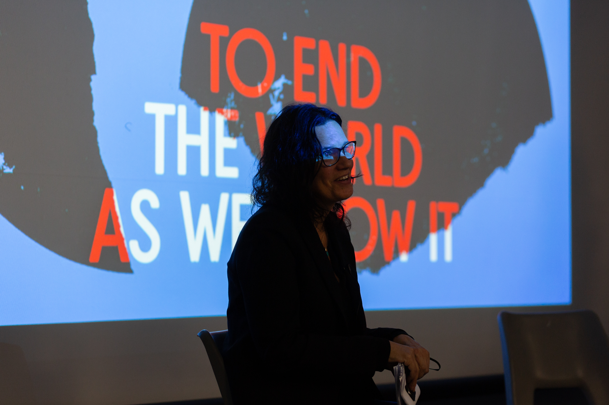 Leanne Betasamosake sits in front of a projected image that reads "TO END THE WORLD AS WE KNOW IT"