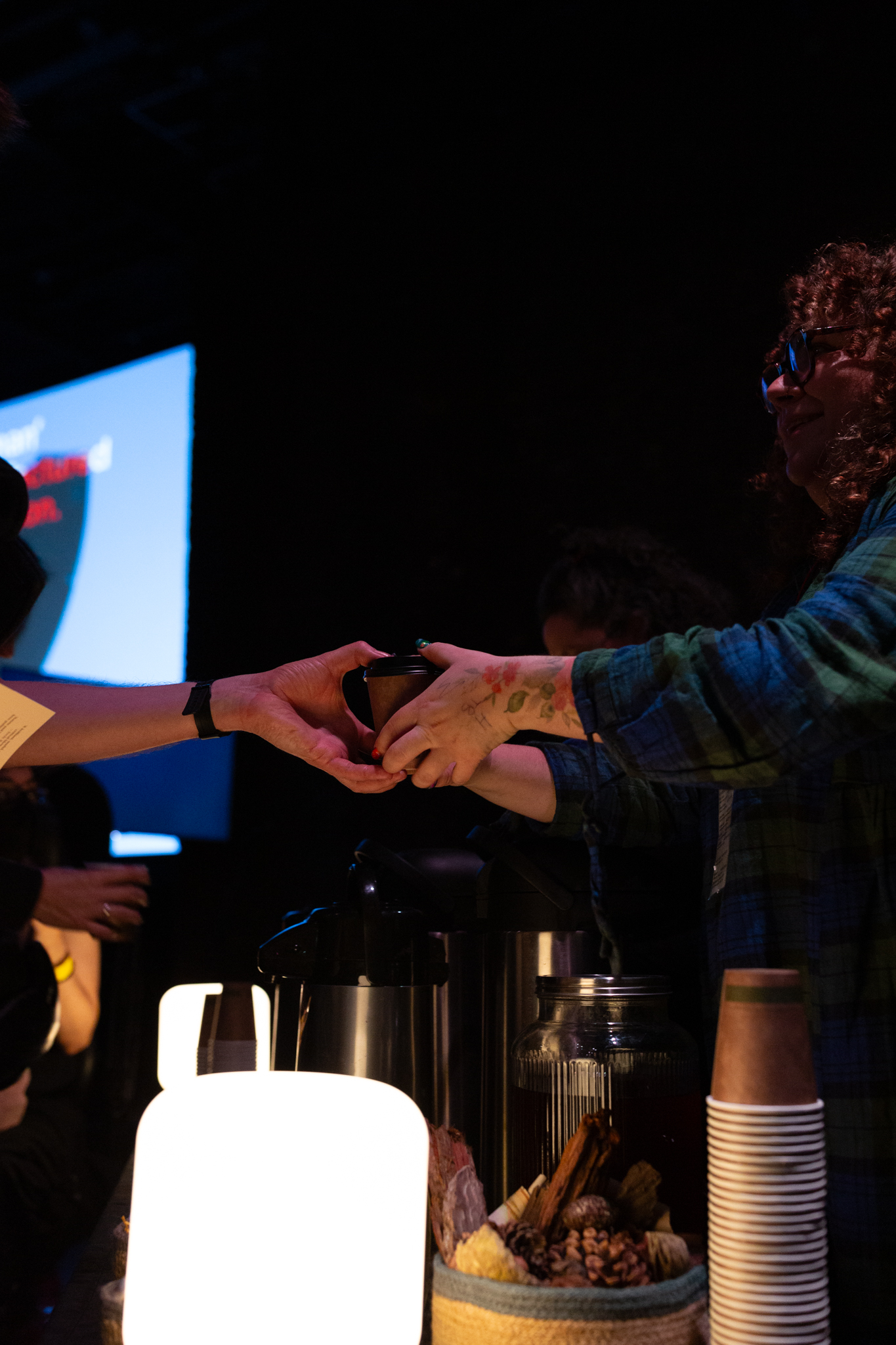 Someone hands a take away cup of Grief Tea to an audience member at Emilia Beatriz's screening of "BARRUNTO"