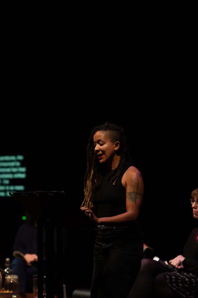 Robyn Maynard stands at a lectern presenting a reading as part of an event.
