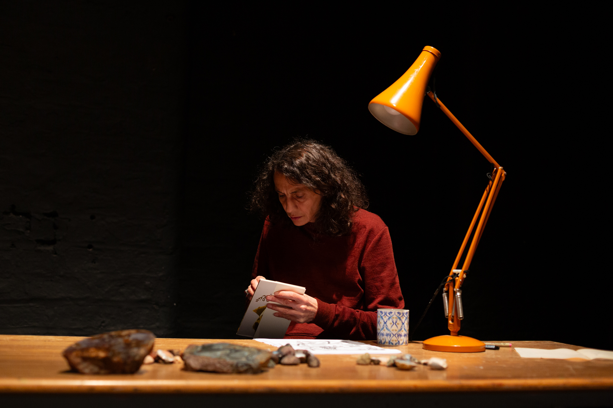 Someone sits at a desk writing in a notebook. On the table is yellow poised desk lamp.