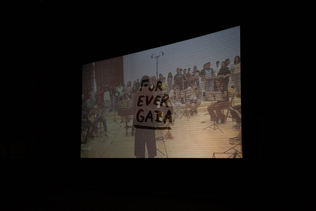 The words "for ever Gaza" are overlayed on an image of an orchestra playing in a brightly lit room.