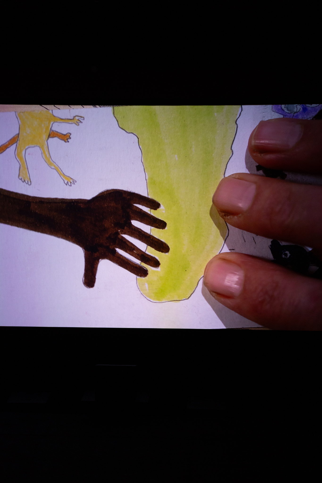 Projected image of fingers sat on top of a child-like drawing of a hand with six fingers on top of a green shape that looks like a map