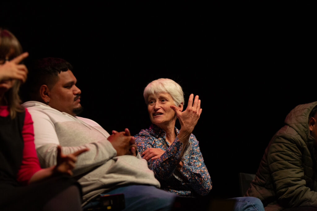 Elizabeth A Povinelli is sat on stage in discussion Kieran Sing. She holds her hand out in front of her in an expressive gesture