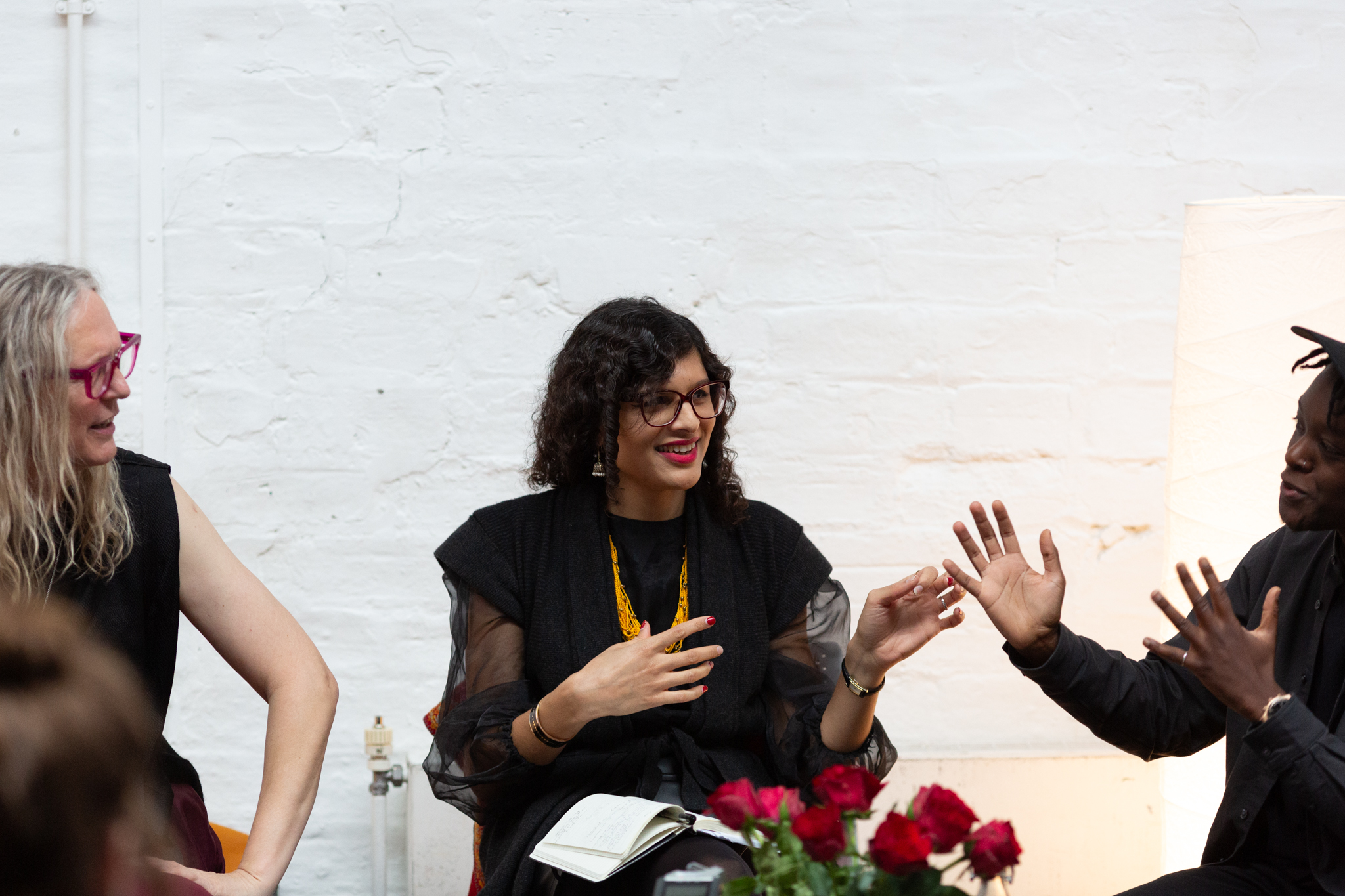 Jay Bernard, Nat Raha and Mijke van der Drift in discussion. Jay Bernard talks while expressively gesturing with their hands whilst looking at Nat who is smiling back at them with hand gestured towards Jay.