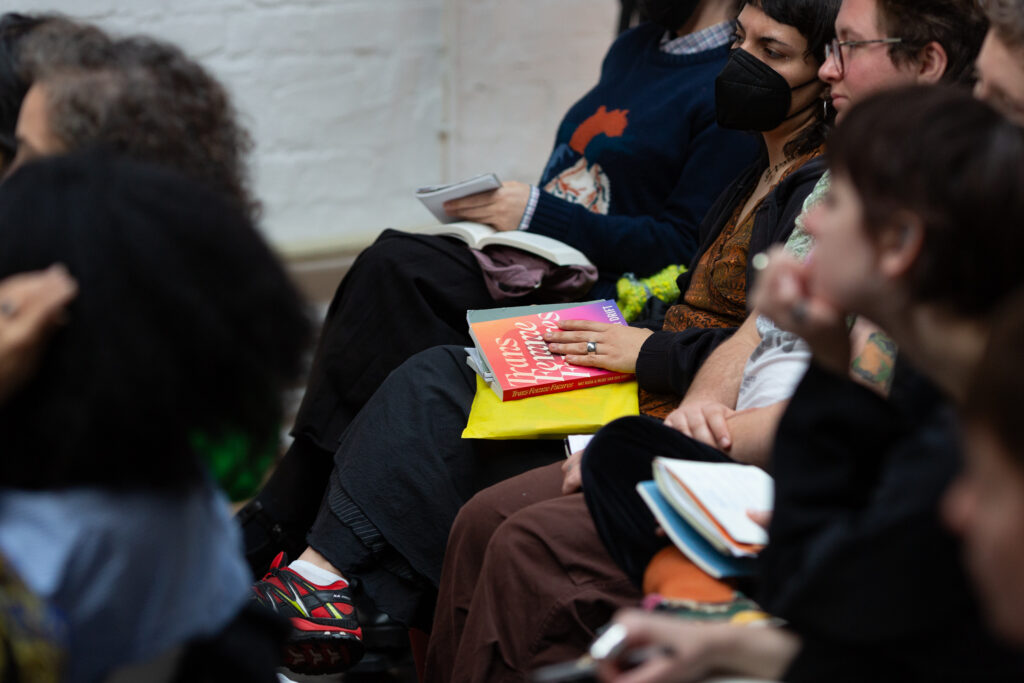 Audience members sit quietly, focused on the event. On one person's lap rests a copy of Trans Femme Futures, its cover visible