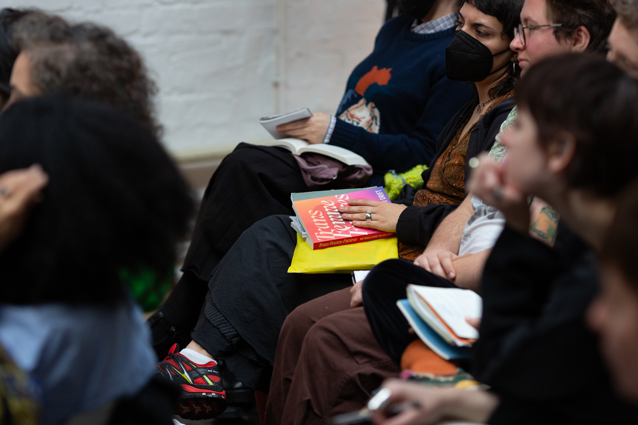 Audience members sit quietly, focused on the event. On one person's lap rests a copy of Trans Femme Futures, its cover visible