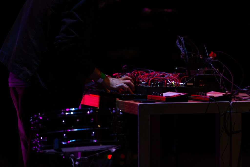 A desk filled with audio equipment and wires. A hand is pressing buttons as though mid movement
