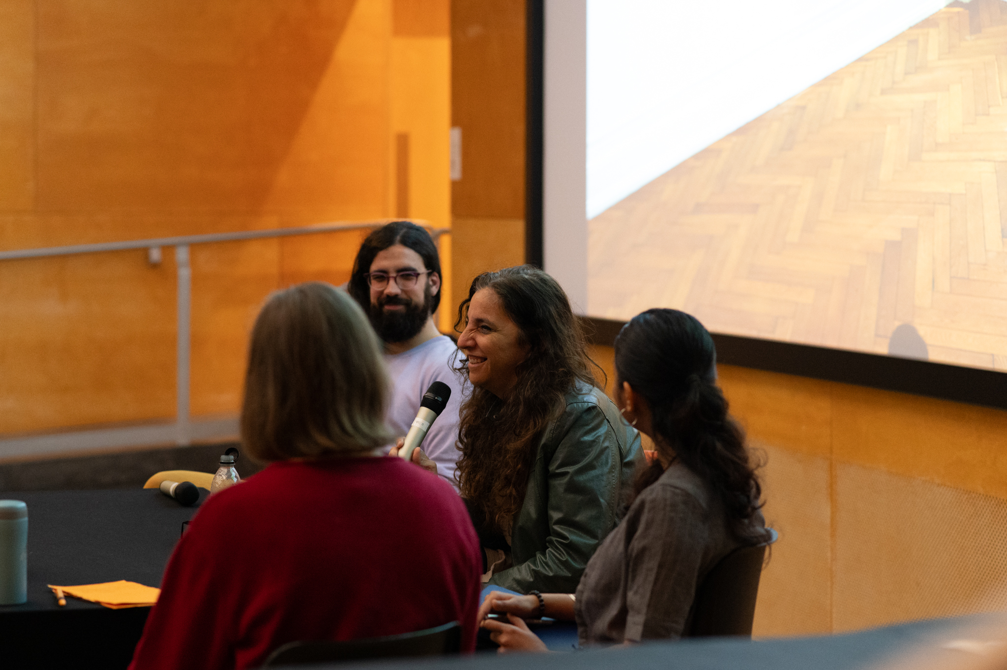 Beatriz Santiago Muñoz sat at a table talking and smiling while holding a microphone. Three other people are sit alongside.