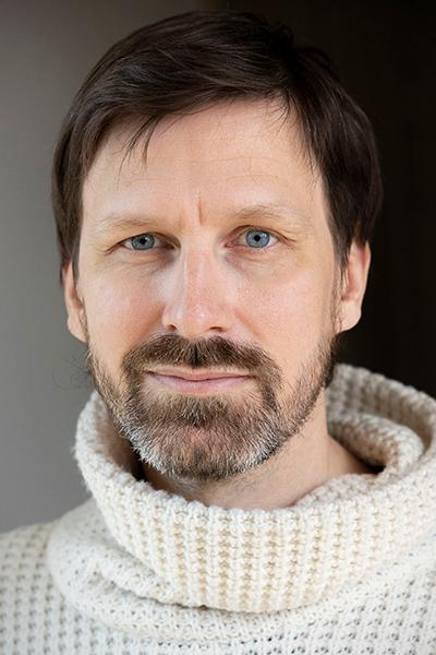 Portrait of Ståle Holgersen looking at the camera with a soft smile. They have dark short hair and a bear,
