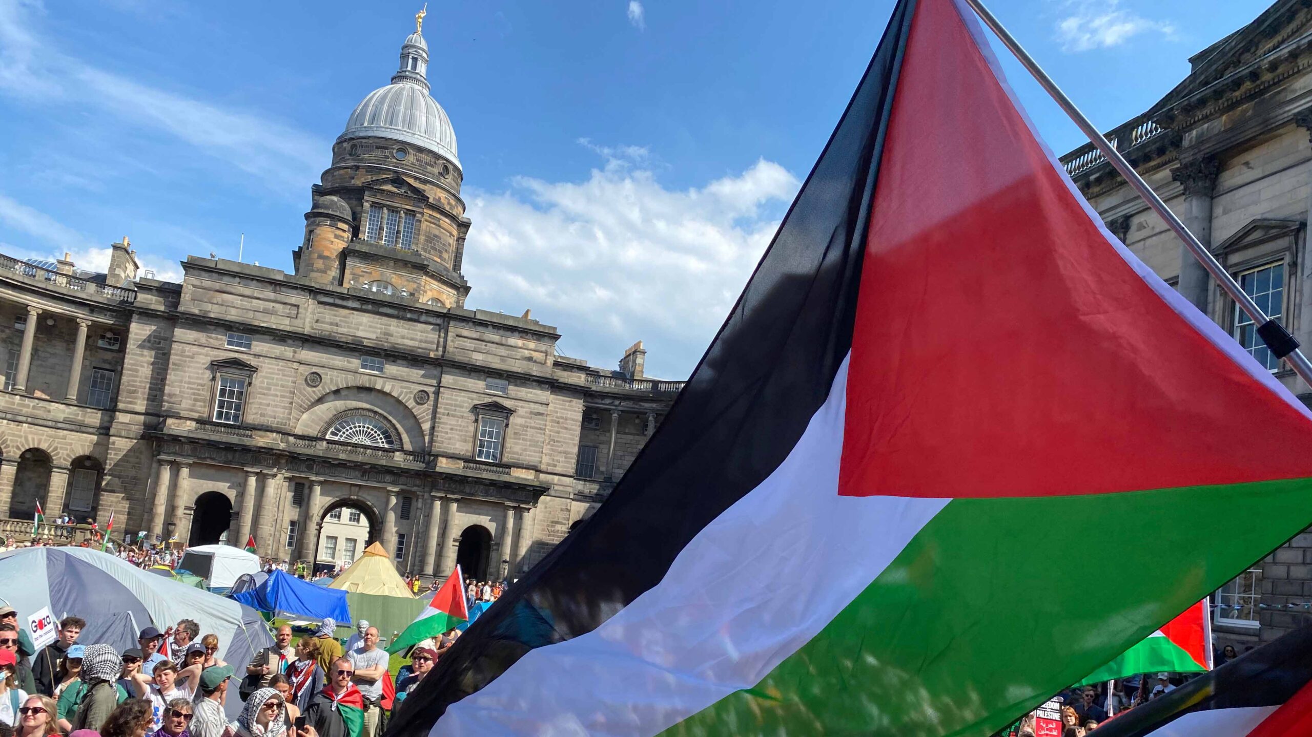 A Palestine flag blowing in the wind during a busy protest at an Edinburgh University campus.