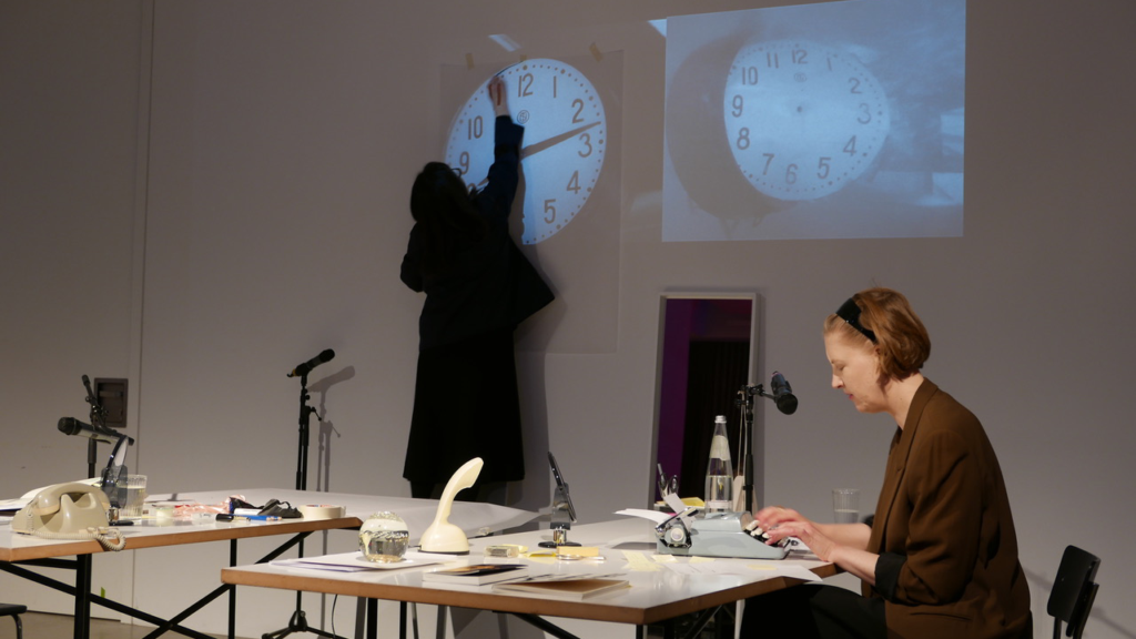 The author/artist is tracing the image of a clock projected onto a tracing paper on the wall.