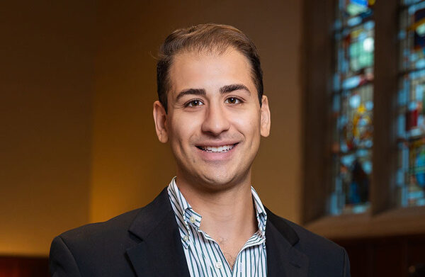 A photo of Peter, a man with light skin brown hair and dark eyes. He wears a striped blue and white shirt and a black blazer